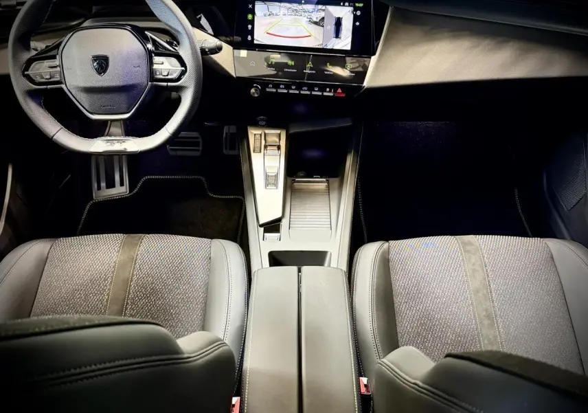 Vue intérieure avant de la Peugeot 308 GT 2025, montrant le volant cuir, la console centrale moderne et les sièges tissu/TEP gris.