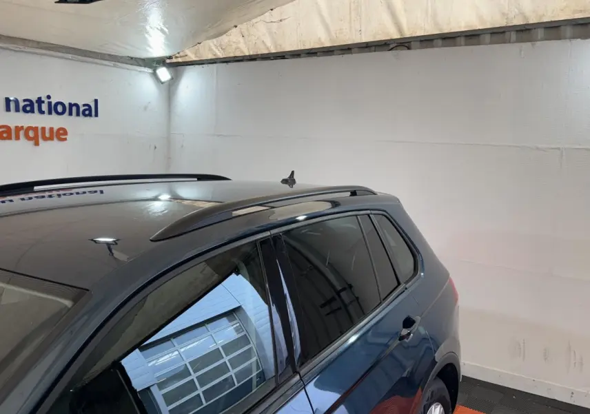 Vue latérale droite d’un Volkswagen Tiguan bleu avec rails de toit noirs dans un garage éclairé.