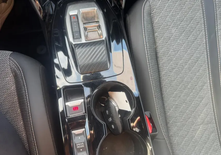 Vue rapprochée de la console centrale noire brillante du Peugeot 2008 Hybrid 145 avec sélecteur de vitesse et porte-gobelets.