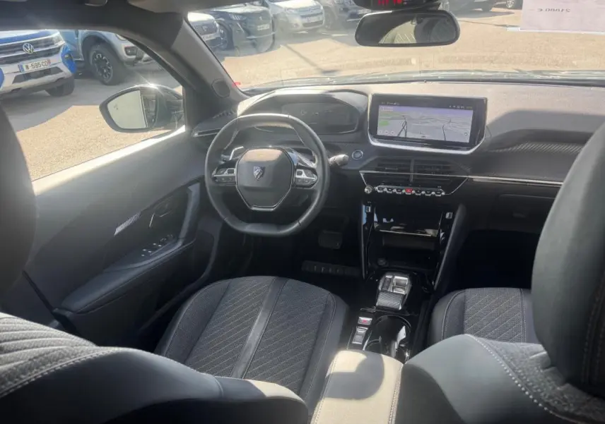 Vue intérieure avant du Peugeot 2008 Hybrid gris, montrant le volant compact, l'écran tactile et les sièges en tissu noir.