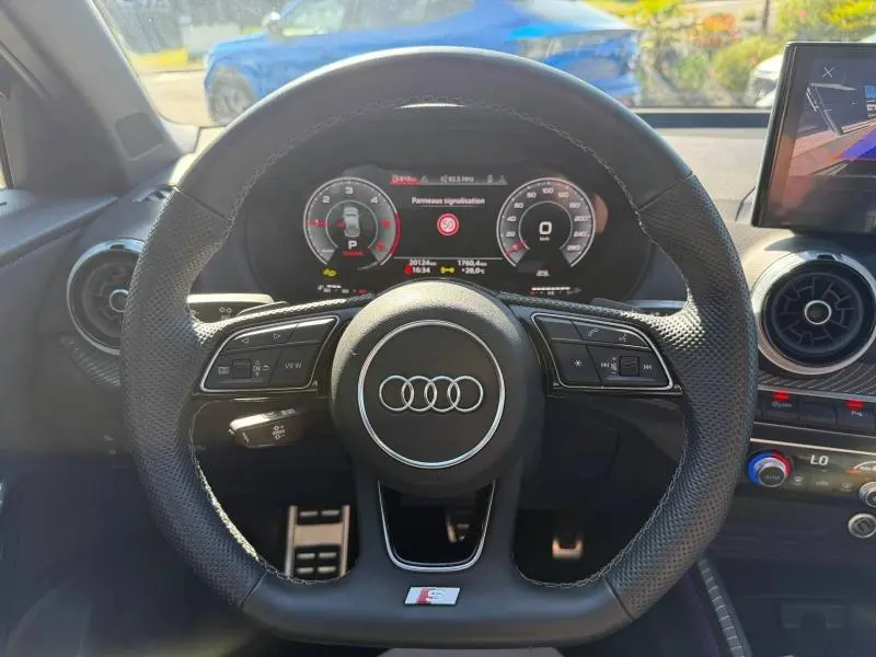 Vue intérieure centrée sur le volant perforé S line d'un Audi Q2 35 TDI gris Daytona avec tableau de bord numérique.