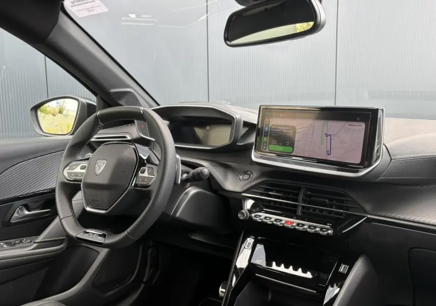 Vue intérieure côté conducteur du Peugeot 208 Hybrid 110 GT 2025, avec tableau de bord numérique et écran tactile central.