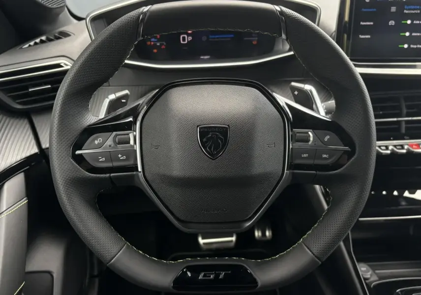 Volant compact cuir noir avec badge GT et commandes intégrées, vue frontale du poste de conduite Peugeot 208 Hybrid 2025.