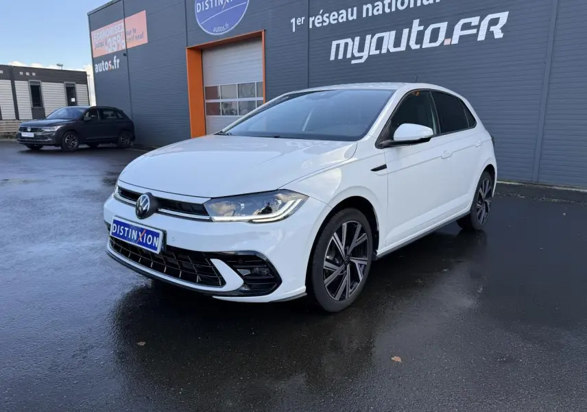 Volkswagen Polo blanc pur vue 3/4 avant droit avec jantes alliage et calandre R-Line devant un bâtiment gris.