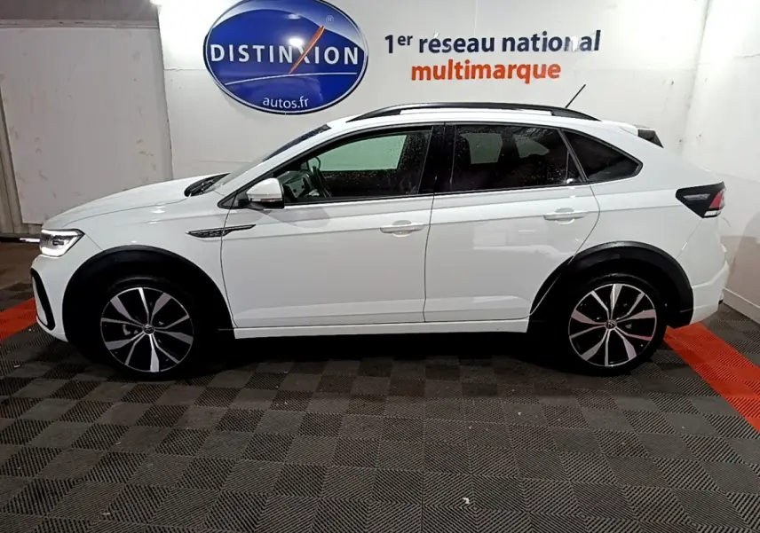 Profil droit d’un Volkswagen Taigo blanc 2022 R-Line avec jantes noires et toit ouvrant visible en intérieur showroom.