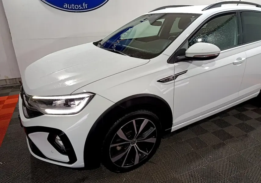 Vue 3/4 avant droite du Volkswagen Taigo blanc 1.0 TSI 110 DSG R-Line avec jantes alliage et feux LED allumés.