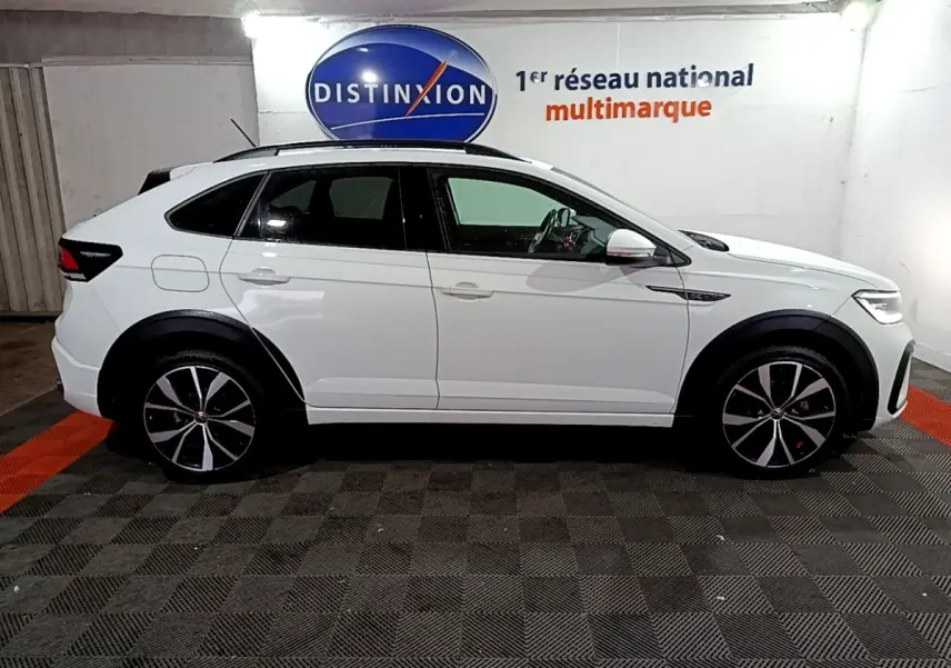 Vue de profil côté gauche d'un Volkswagen Taigo blanc 2022 R-Line avec jantes noires et toit noir dans un garage.