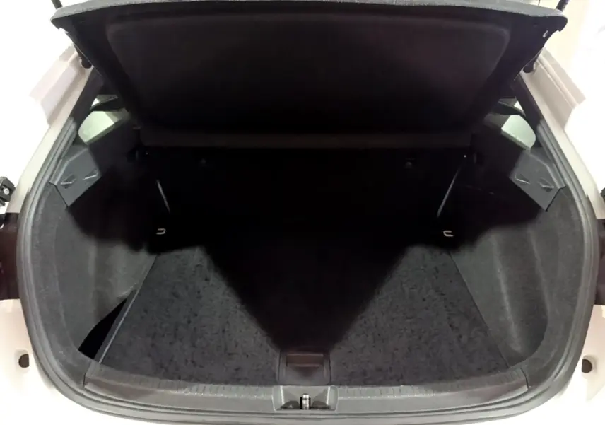 Vue du coffre ouvert d'une Volkswagen Taigo blanc, montrant l'espace de rangement intérieur vide et la tablette arrière relevée.