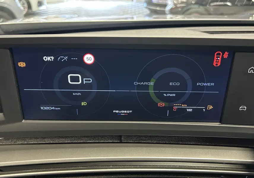 Tableau de bord numérique du Peugeot 5008 gris Artense, affichage vitesse, charge hybride et alertes visibles.