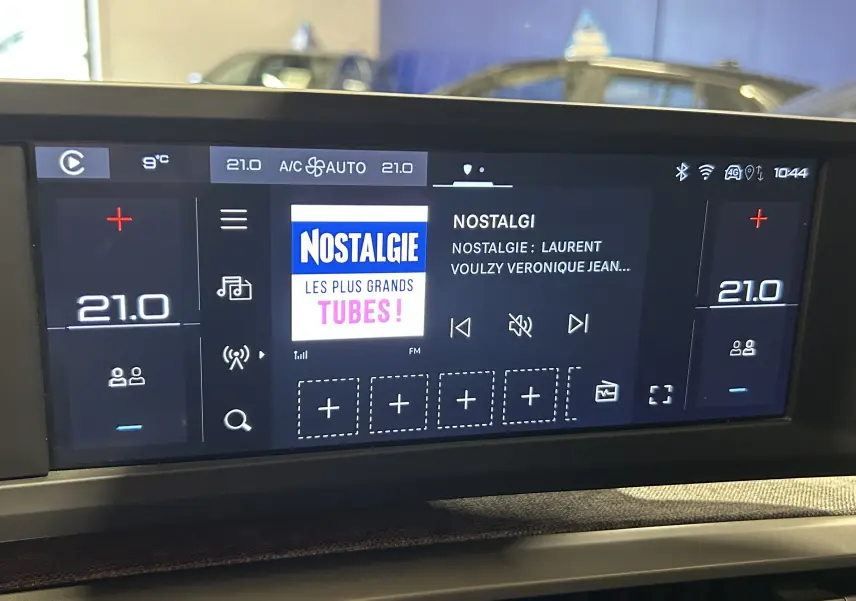 Écran tactile central du tableau de bord de la Peugeot 5008 III Hybrid, affichant la radio et la climatisation à 21°C.