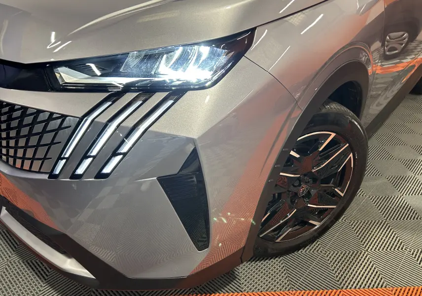Gros plan sur l'avant droit gris Artense du Peugeot 5008 III Hybrid, mettant en valeur le phare LED et la jante noire.