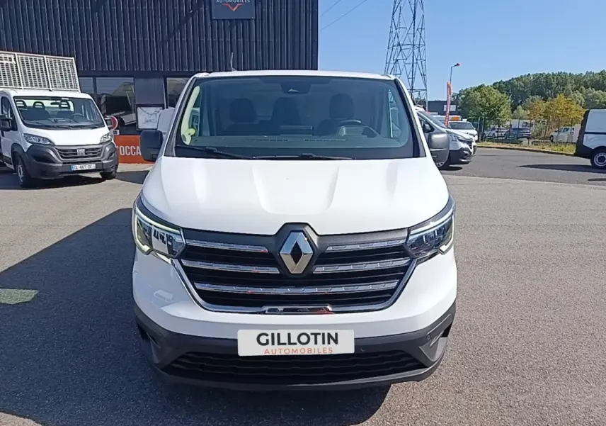 Vue avant d’un Renault Trafic Fourgon blanc 2023 avec calandre chromée et phares LED allumés.