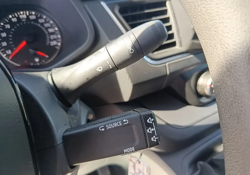 Détail du commodo gauche noir avec commandes audio sur le volant d'un Renault Trafic Fourgon blanc, intérieur gris.