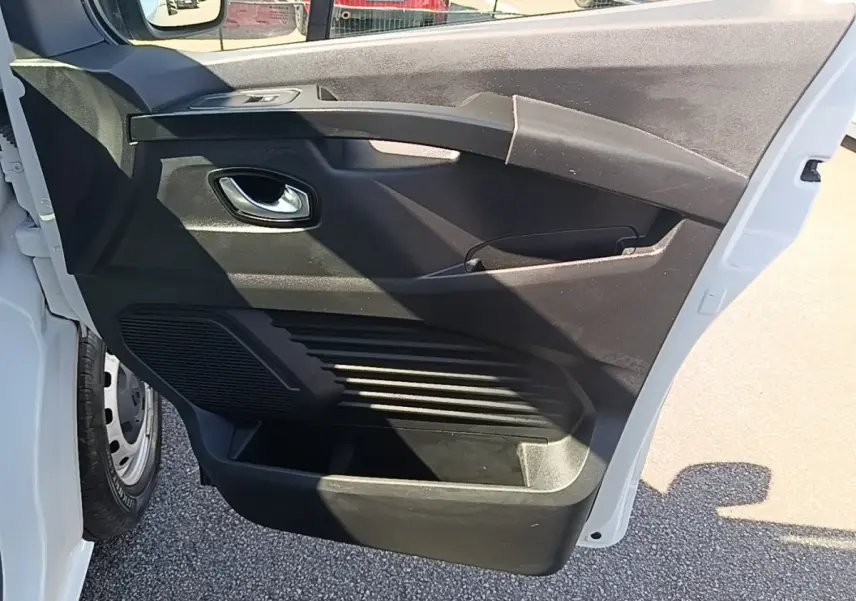 Vue rapprochée de la porte avant gauche ouverte du Renault Trafic Fourgon blanc, montrant la poignée intérieure et les rangements.
