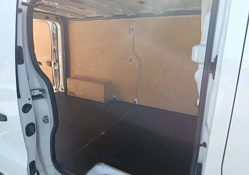 Vue intérieure côté droit du fourgon blanc Renault Trafic avec cloison bois et plancher noir antidérapant.