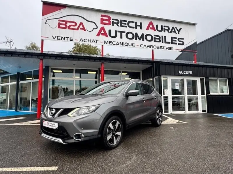 Nissan Qashqai gris Squale en 3/4 avant droit devant un garage Brech Auray Automobiles par temps couvert.