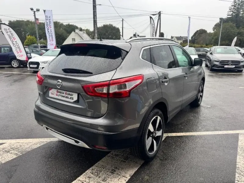 Nissan Qashqai gris Squale vu 3/4 arrière droit sur parking, avec jantes alliage et becquet arrière visible.