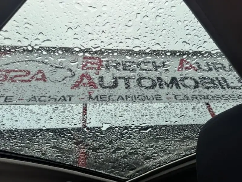 Vue intérieure du toit ouvrant d'un Nissan Qashqai gris sous pluie, avec gouttes d'eau visibles sur le verre.