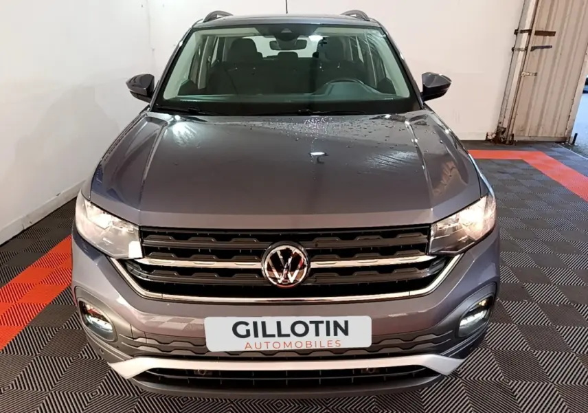 Vue avant d'un Volkswagen T-Cross gris foncé 2023 avec calandre chromée et feux allumés en intérieur.