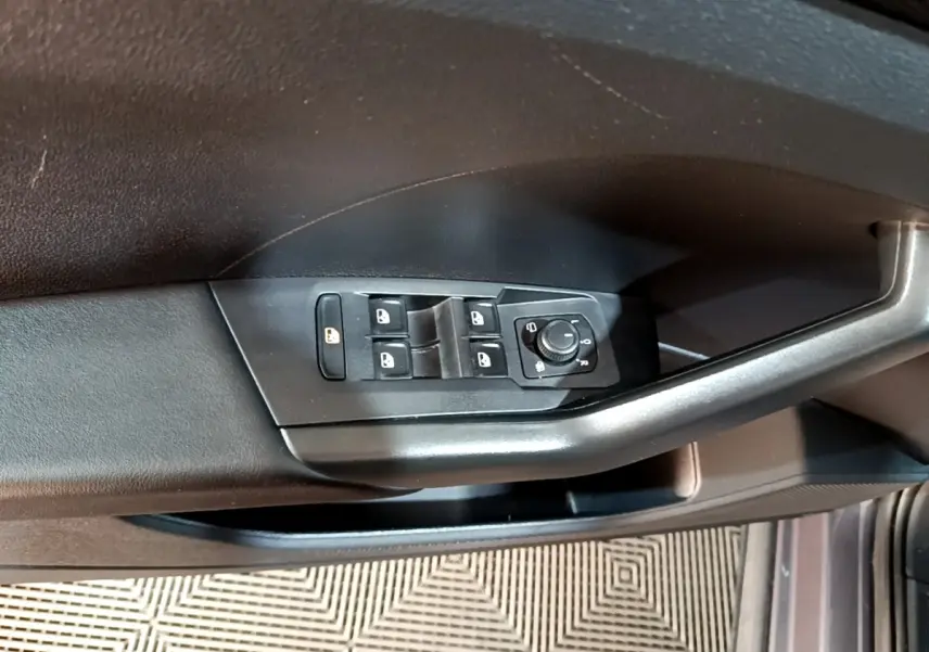 Vue rapprochée des commandes de lève-vitres et réglage des rétroviseurs sur la porte côté gauche du Volkswagen T-Cross gris foncé.