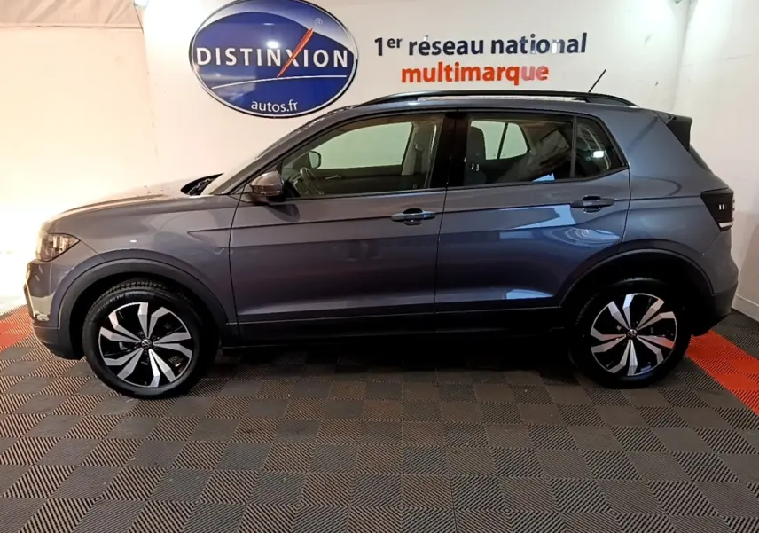 Vue de profil côté gauche d'un Volkswagen T-Cross gris foncé 2023 avec jantes alliage bicolores et barres de toit noires.