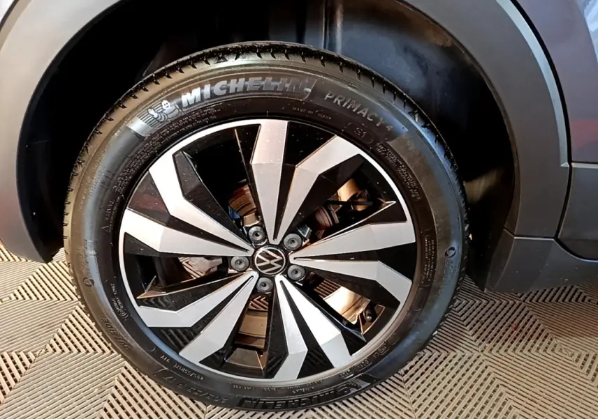 Gros plan sur la roue avant droite du Volkswagen T-Cross gris foncé, jante alliage bicolore au design géométrique.