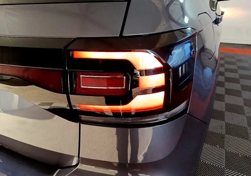 Gros plan sur le feu arrière droit allumé d’un Volkswagen T-Cross gris foncé, avec reflets sur la carrosserie.