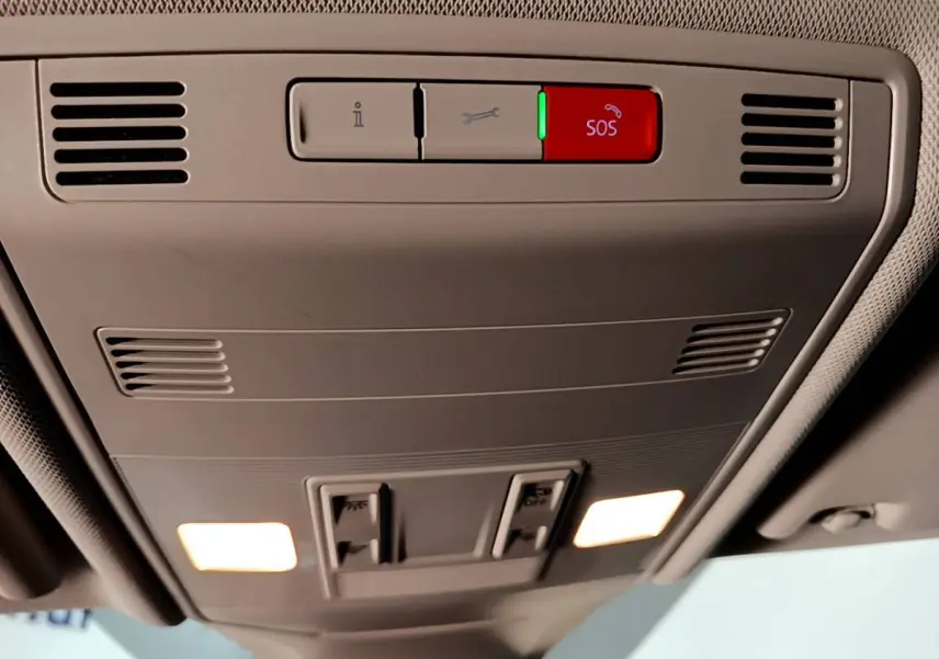 Vue en contre-plongée du panneau de commande de toit intérieur gris clair du Volkswagen T-Cross 2023 avec bouton SOS rouge éclairé.