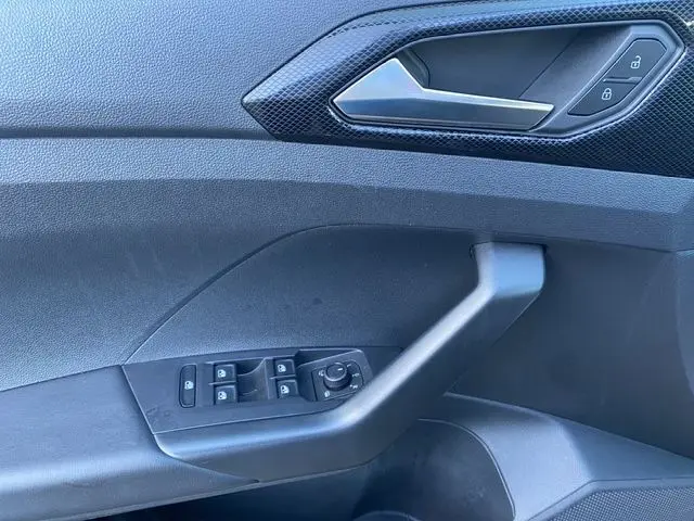 Détail de la porte côté conducteur du Volkswagen T-Cross noir 2025, montrant les commandes des vitres et la poignée intérieure.