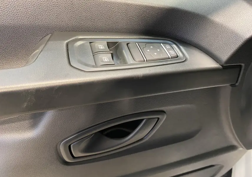 Gros plan sur la commande des vitres électriques et le bouton de réglage des rétroviseurs côté conducteur d’un Renault Trafic blanc.