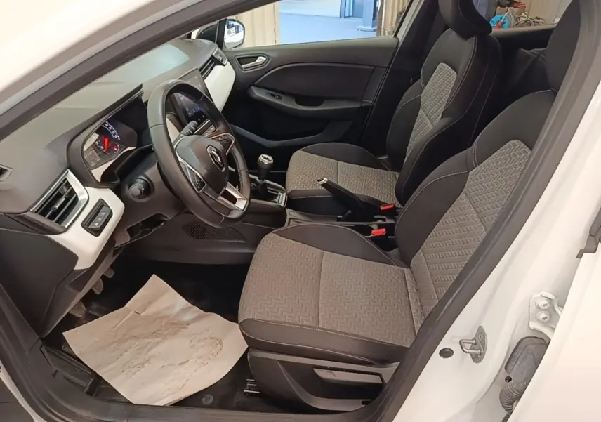 Intérieur avant droit de la Renault Clio blanche 2023, montrant sièges tissu bicolore et volant multifonctions cuir synthétique.