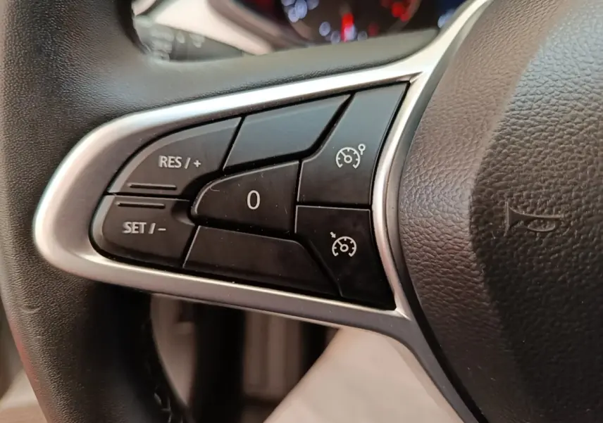 Gros plan sur les commandes du régulateur de vitesse au volant cuir synthétique d'une Renault Clio blanche 2023.