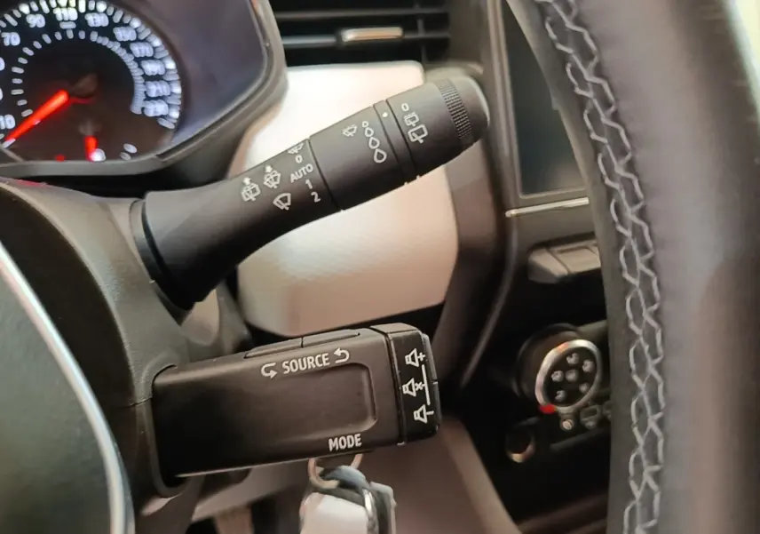 Gros plan sur les commandes au volant cuir synthétique de la Renault Clio 2023, avec tableau de bord partiellement visible.