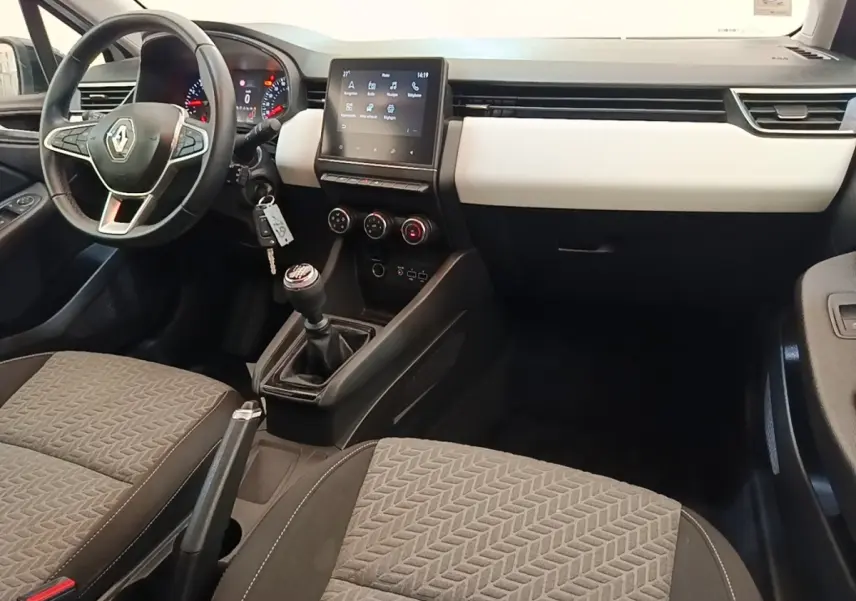 Intérieur de Renault Clio 2023 blanc, vue avant centrée sur tableau de bord, volant cuir et écran tactile central.