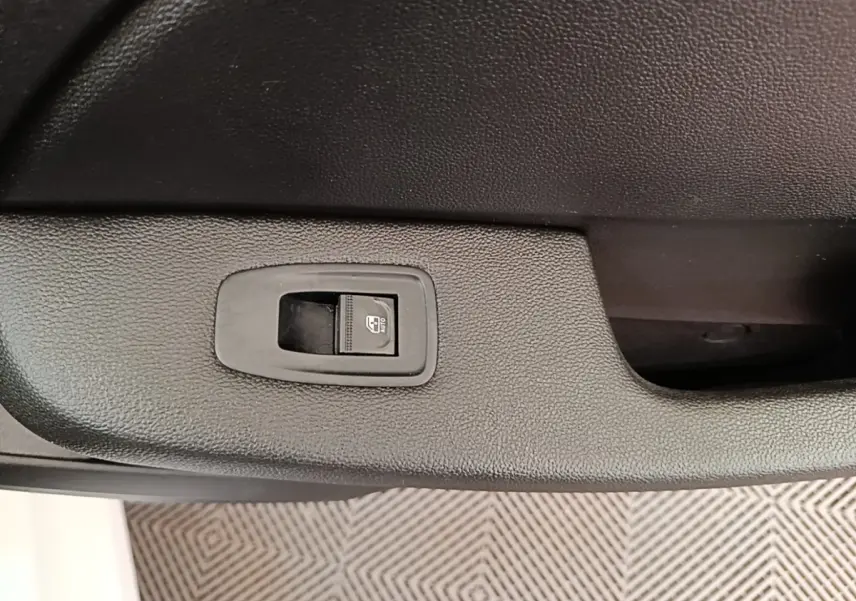 Gros plan sur le bouton de commande de la vitre électrique côté conducteur dans une Renault Clio blanche 2023.