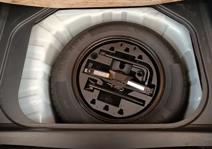 Roue de secours avec outillage intégré dans le coffre d'une Renault Clio blanche, vue de dessus.