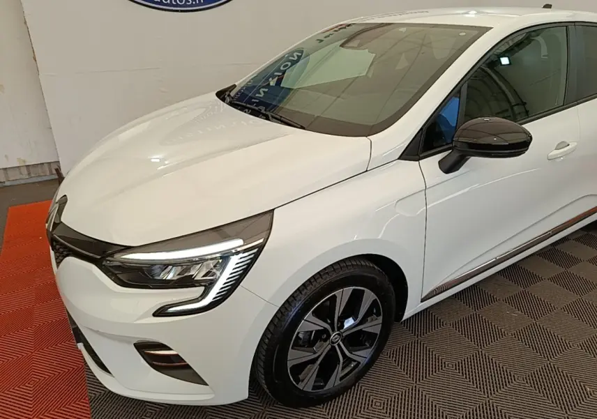 Renault Clio 2023 blanche vue 3/4 avant droit, avec phares LED et jantes alliage noires distinctives.