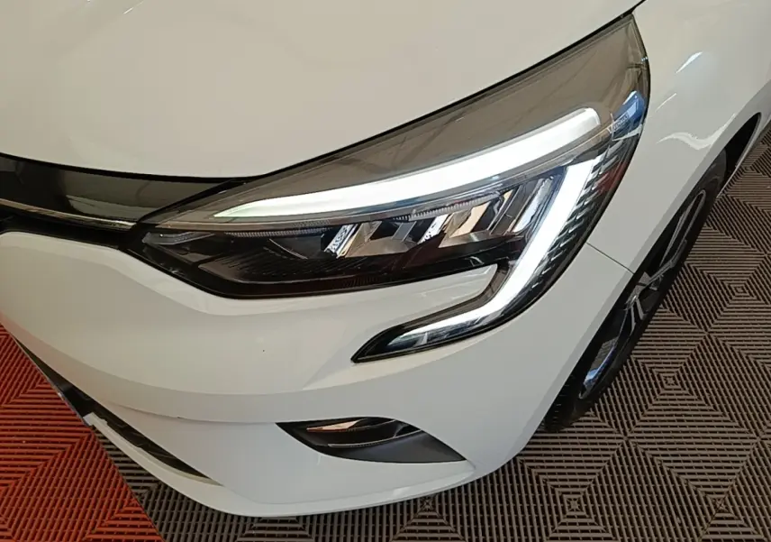 Gros plan sur le phare avant droit blanc de la Renault Clio 2023 avec éclairage LED et partie de la calandre visible.