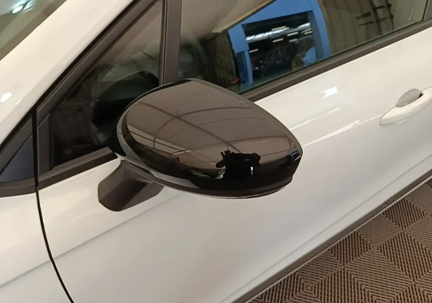Gros plan sur le rétroviseur noir côté gauche d'une Renault Clio blanche, vue partielle de la porte avant.