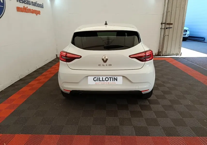 Vue arrière d'une Renault Clio blanche 2023 garée en intérieur avec feux arrière LED allumés.
