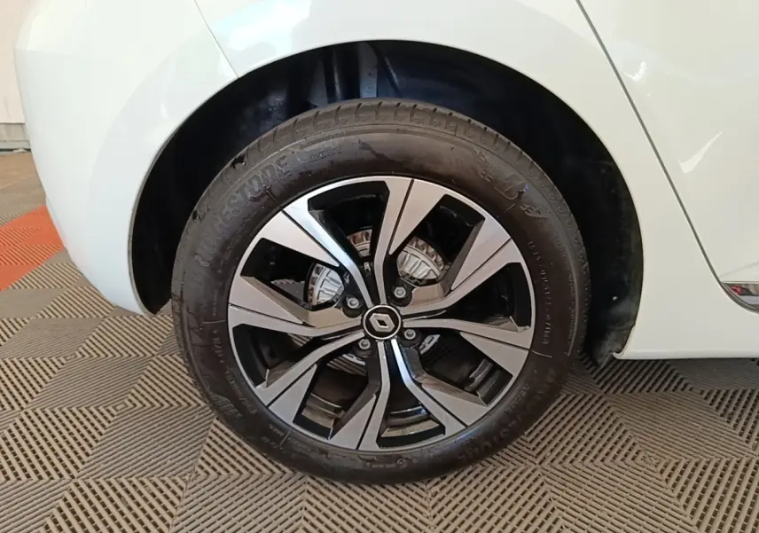 Gros plan sur la roue arrière droite d'une Renault Clio blanche, avec jante alliage bicolore et logo Renault central.