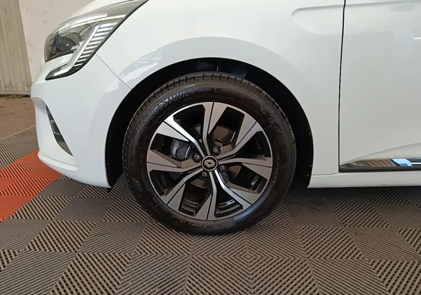 Gros plan sur la roue avant gauche d'une Renault Clio blanche 2023 avec jante alliage noire et argentée.