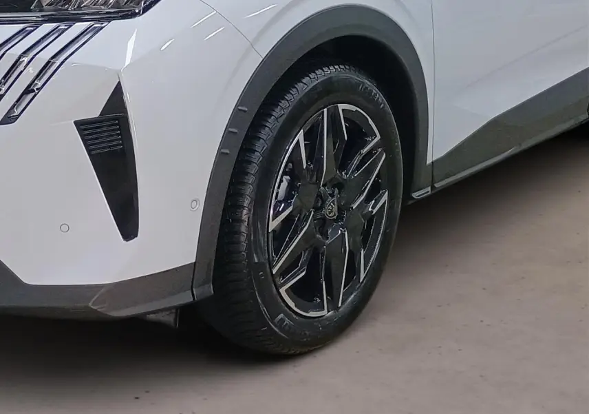 Gros plan sur le volant noir cuir avec commandes intégrées et partie gauche du tableau de bord gris clair du Peugeot 3008 Hybrid 2025.