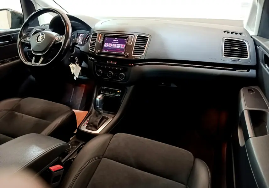 Vue intérieure côté conducteur du Volkswagen Sharan 2017, tableau de bord noir avec écran tactile et volant cuir multifonctions.