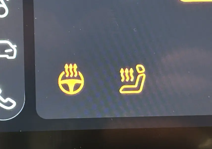 Icônes orange allumées du volant chauffant et du siège chauffant sur l'écran de bord d'une MG ZS blanche.