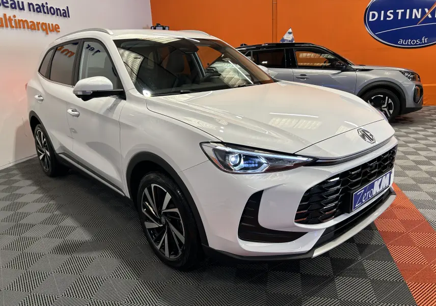 Vue 3/4 avant droite du SUV MG ZS 1.5 Hybrid+ Dover White avec calandre noire et phares LED allumés.