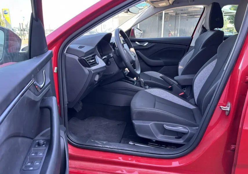 Intérieur côté conducteur d'une Skoda Scala rouge velvet metal 2024, sièges tissu noir et gris, volant multifonctions visible.