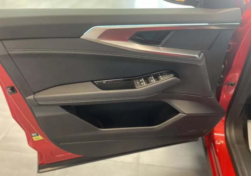 Porte avant gauche rouge avec garniture intérieure noire, surpiqûres blanches et commandes électriques des vitres.