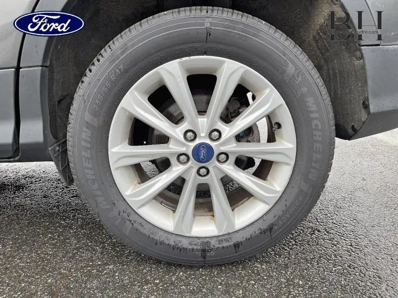 Gros plan sur la roue avant droite du Ford Kuga gris Magnetic, jante alliage 10 branches avec logo Ford central.