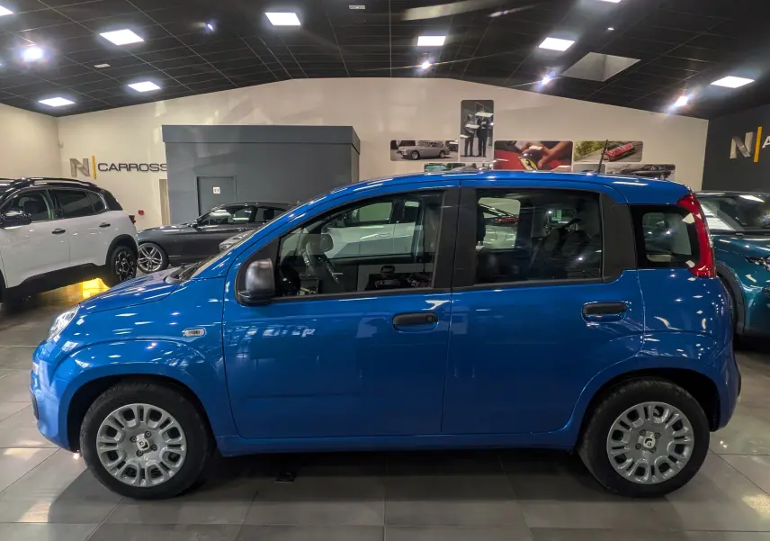 Profil côté gauche d'une Fiat Panda 1.0 Hybrid City 2025 en Bleu Italia dans un showroom lumineux.